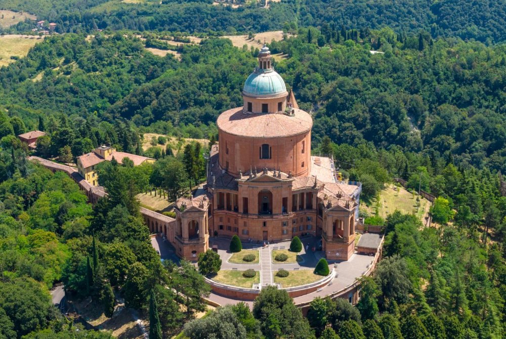 Luchtfoto van het barokke heiligdom van Onze-Lieve-Vrouw van San Luca bovenop Monte della Guardia, omgeven door beboste heuvels in de buurt van Bologna